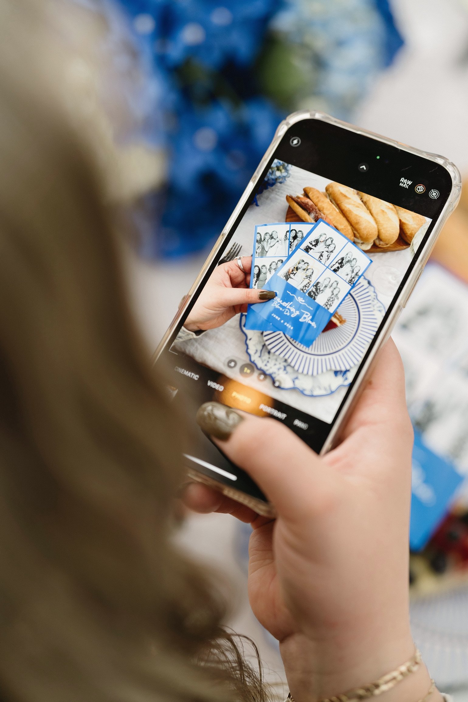 A phone camera framing two photo booth strips held over a table set with food